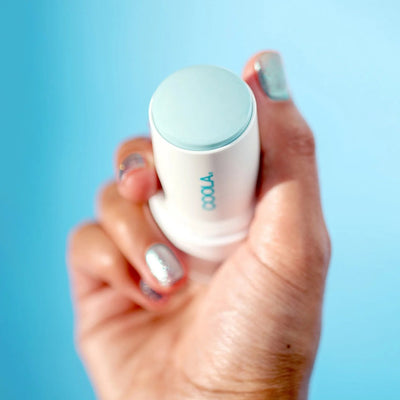 Hand holding a Refreshing Water Hydration Stick SPF 50 against a blue background, showcasing organic sunscreen protection.