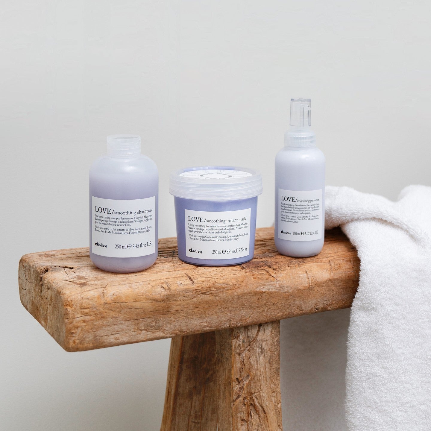 Davines Love Smoothing Hair Products on Wooden Bench with White Towel - Shampoo, Conditioner, Perfector
