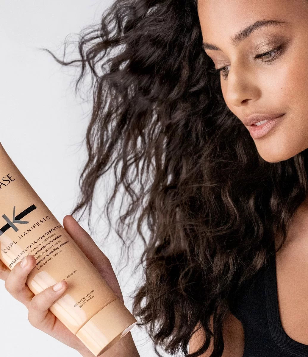Girl with curly hair holding a Kérastase curl manifesto product