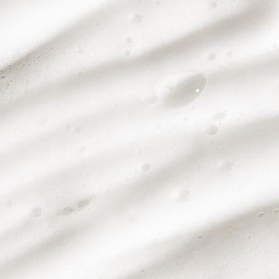 Close-up of white foamy texture with drops of moisture, resembling a gentle exfoliating mousse.