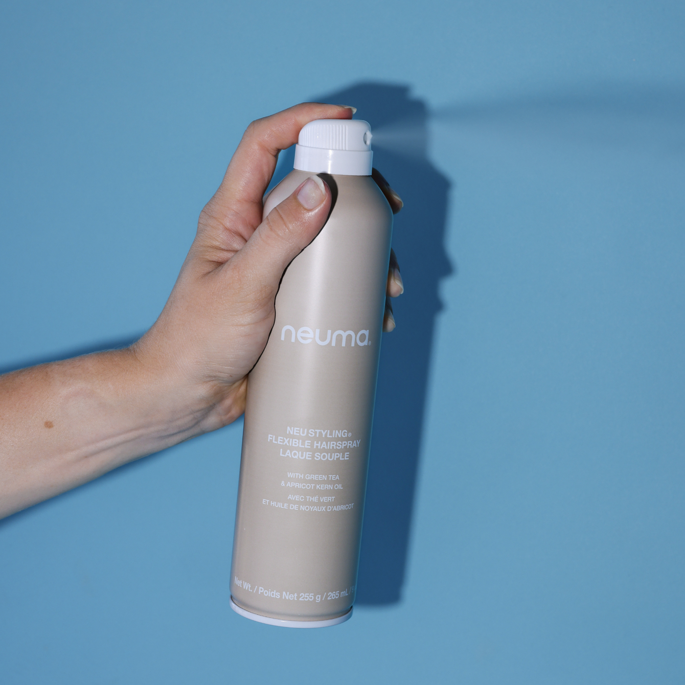 Hand holding Neu Styling Flexible Hairspray can against a blue background, showcasing its lavender, mandarin, and vanilla aroma.