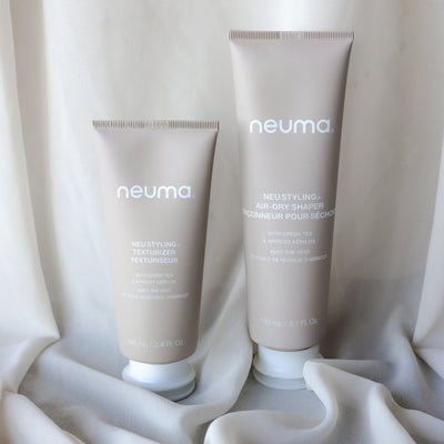 Neuma Neu Styling Air-dry Shaper and Texturizer tubes on a soft fabric background, enhancing natural hair texture and shine.