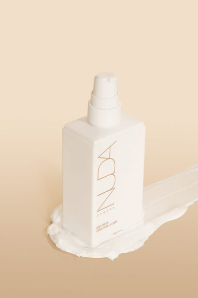 Nuda Routine Kit Body Cream bottle with pump on a creamy backdrop for a radiant tan.