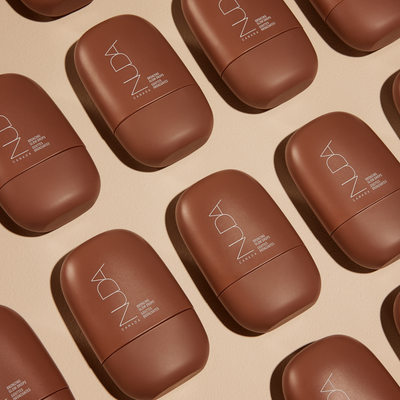 Nuda Bronzing Glow Drops in sleek brown packaging arranged on a light surface for a stylish display.