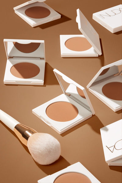 Makeup scene featuring bronzing powder compacts with a soft brush on a warm-toned background, ideal for flawless application.