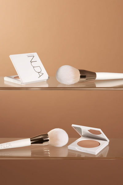 Bronzing powder brush with soft bristles alongside a compact powder against a warm backdrop, perfect for flawless makeup application.