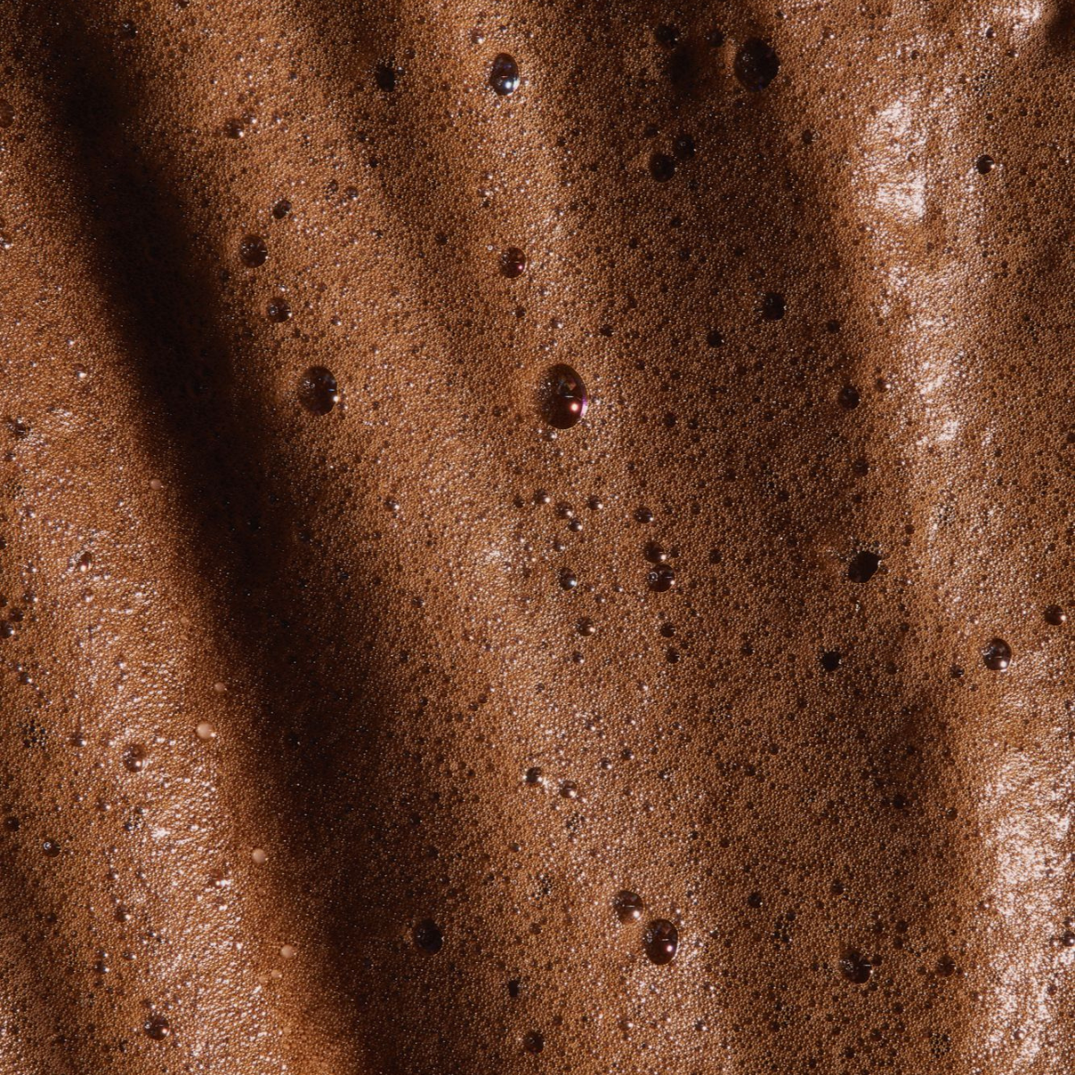 Close-up of rich, dark self-tanning mousse with bubbly texture, perfect for a natural-looking tan.