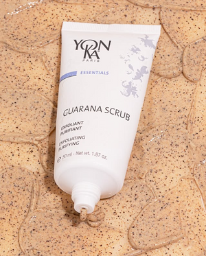 An open bottle of Yonka Guarana Scrub is laying on a table covered in the guarana scrub. 