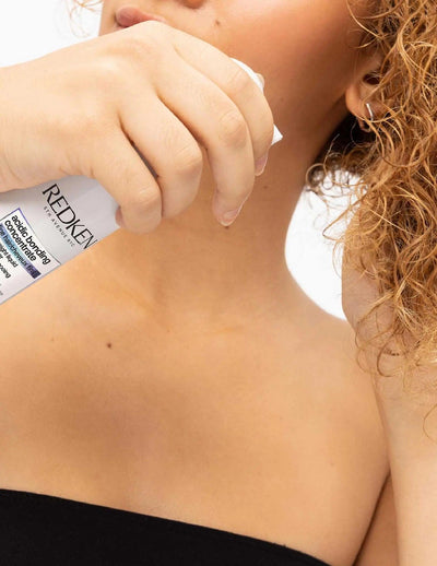 Woman applying Redken Acidic Bonding Lightweight Liquid Conditioner for strong, shiny hair.