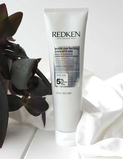 Redken Acidic Perfecting Concentrate Leave-in Treatment tube on a textured background, designed for hair restoration and shine.