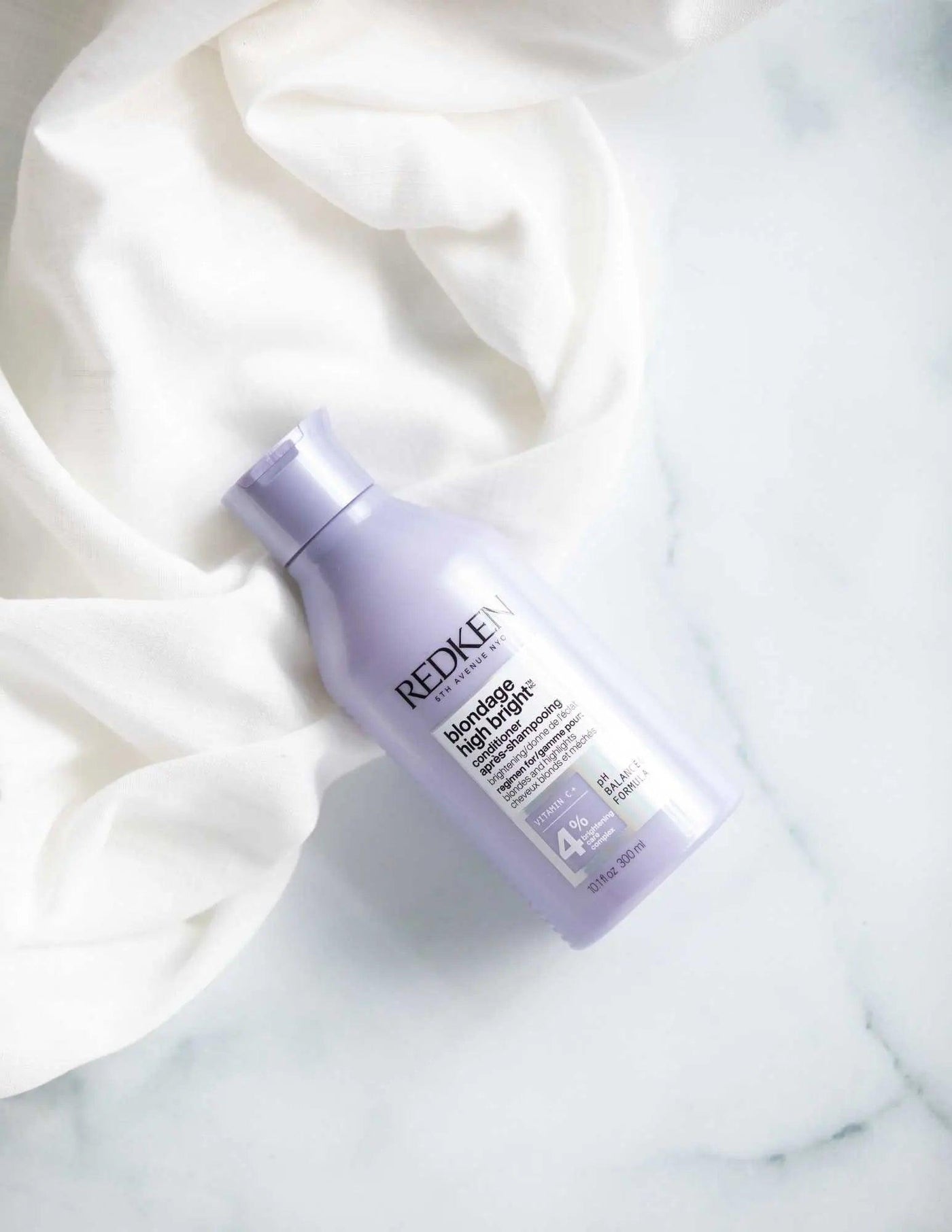 Redken Blondage High Bright Conditioner bottle on a soft white fabric, ideal for enhancing blonde hair vibrancy.