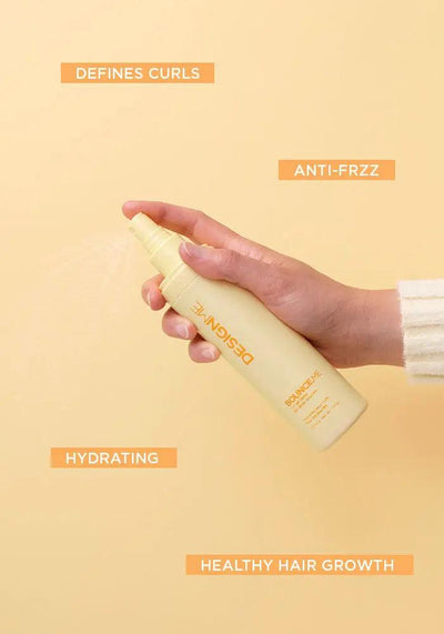 Hand holding a yellow spray bottle labeled "Defines Curls," "Anti-Frizz," "Hydrating," and "Healthy Hair Growth" on a light background.