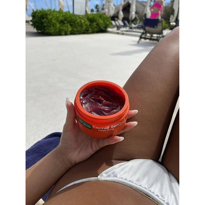 Carrot Cream tanning product displayed in a person's hand at a sunny beach setting.