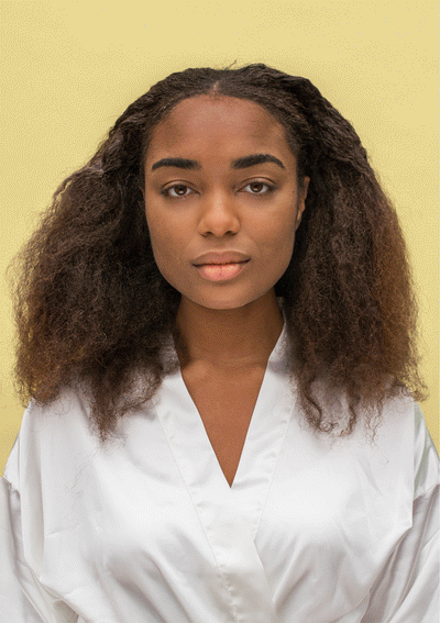 Woman with natural curls showcasing healthy hair texture and volume, wearing a white robe against a yellow backdrop.