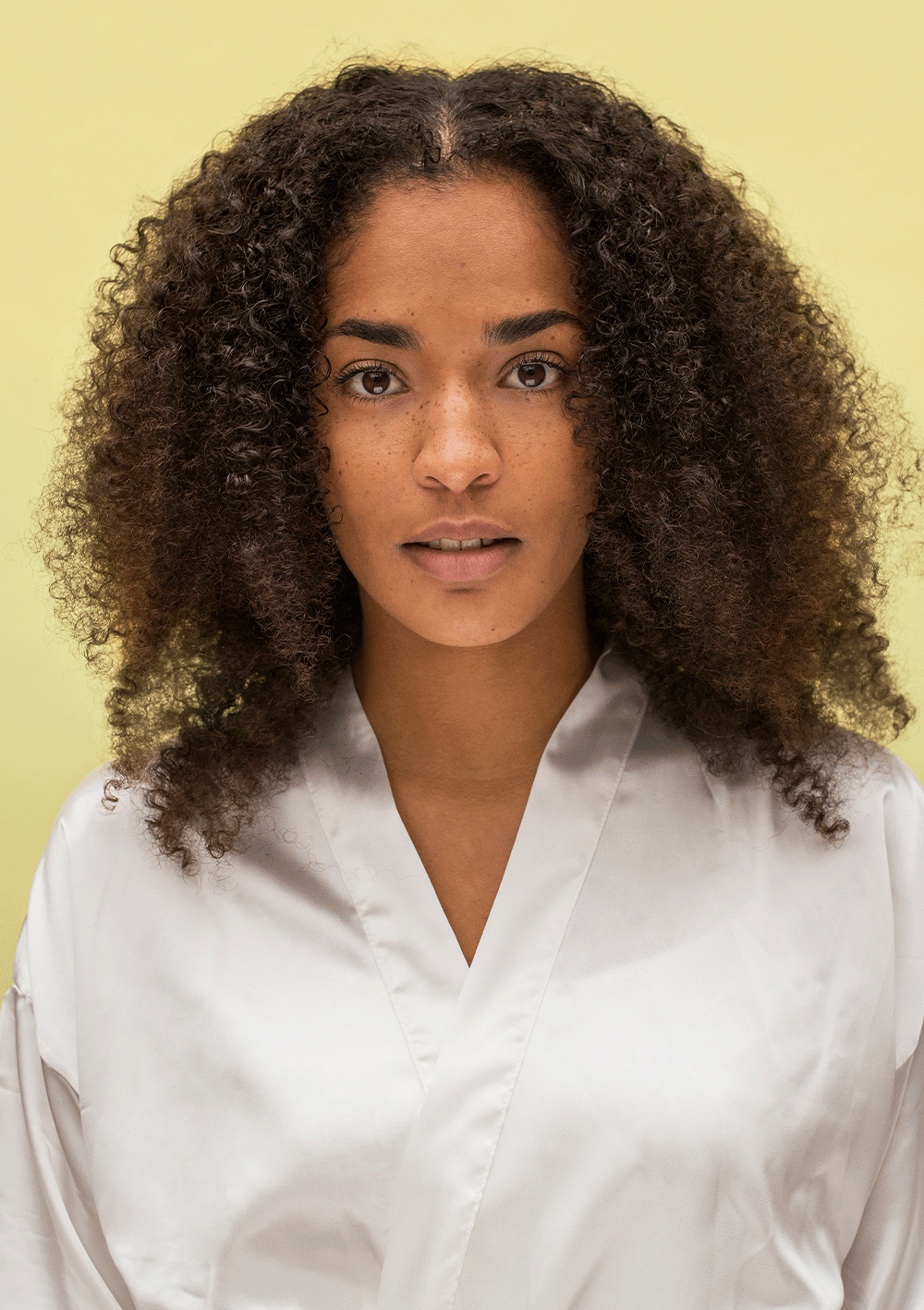 Model with natural curls wearing a silk robe against a light background, showcasing the beauty of defined, bouncy curls.