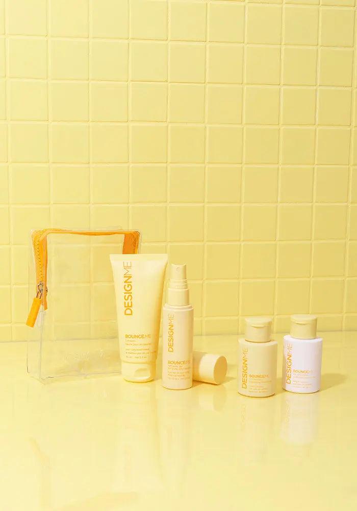 Curl Discovery Kit featuring BOUNCE.ME shampoo, conditioner, curl balm, spray gel, and a clear pouch against a yellow background.