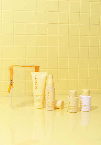 Curl Discovery Kit featuring BOUNCE.ME shampoo, conditioner, curl balm, spray gel, and a clear pouch against a yellow background.