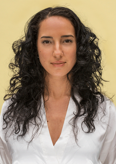 Woman with defined, bouncy curls wearing a white blouse against a yellow background, showcasing vibrant curly hair.