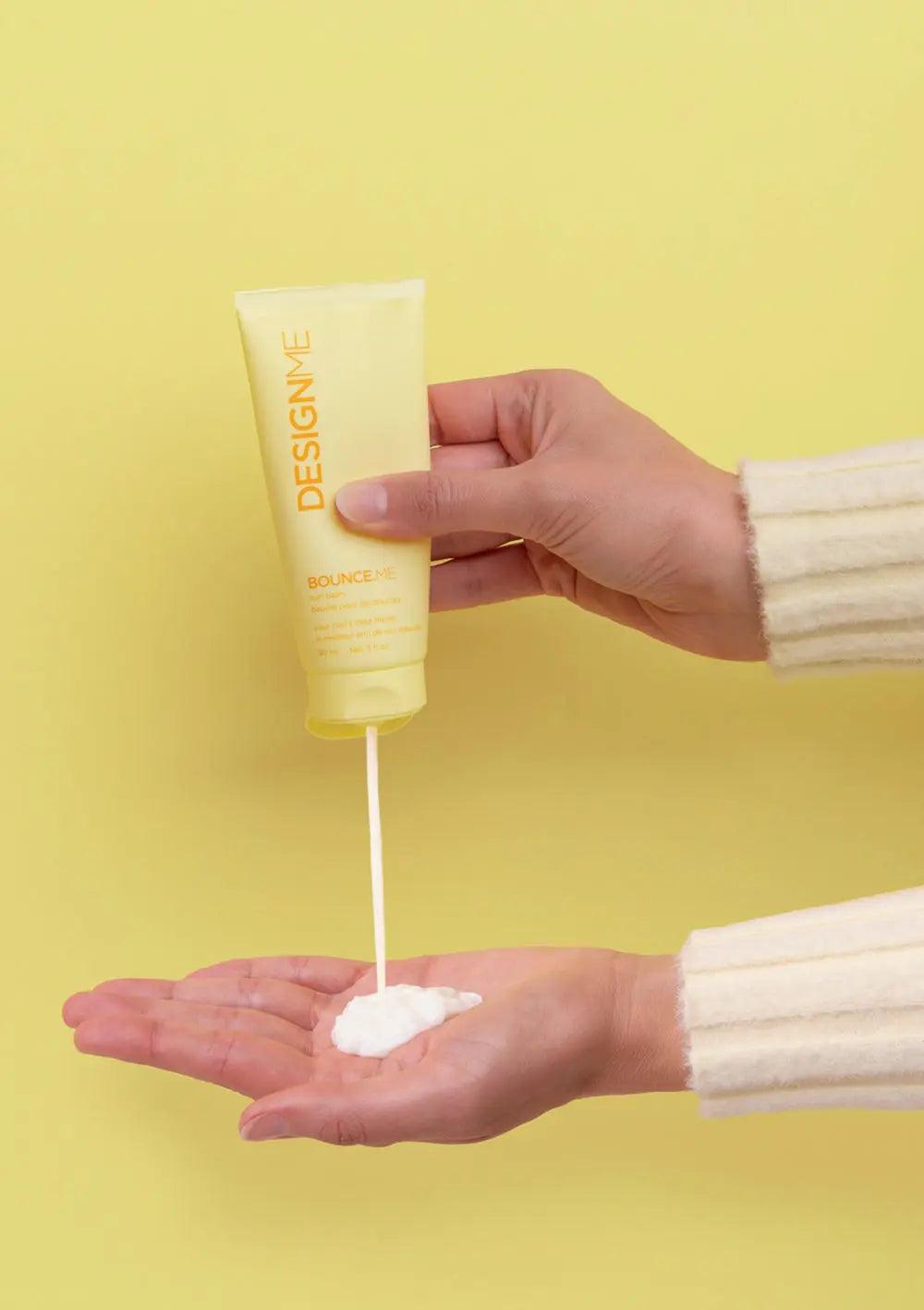 Hand pouring BOUNCE.ME curl balm into palm against a bright yellow background.