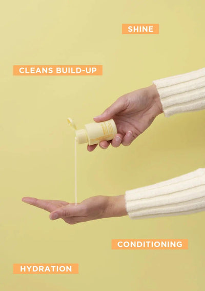 Hand pouring curl shampoo from a yellow bottle, showcasing hydration and shine benefits on a pastel background.