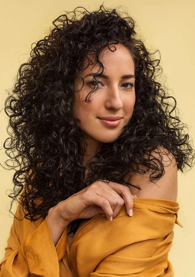 Woman with beautiful curly hair wearing a yellow blouse against a warm background, showcasing healthy curls.