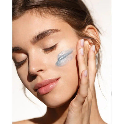 Young woman applying blue deep peeling cream on her face for smooth, renewed skin and deep pore cleansing.