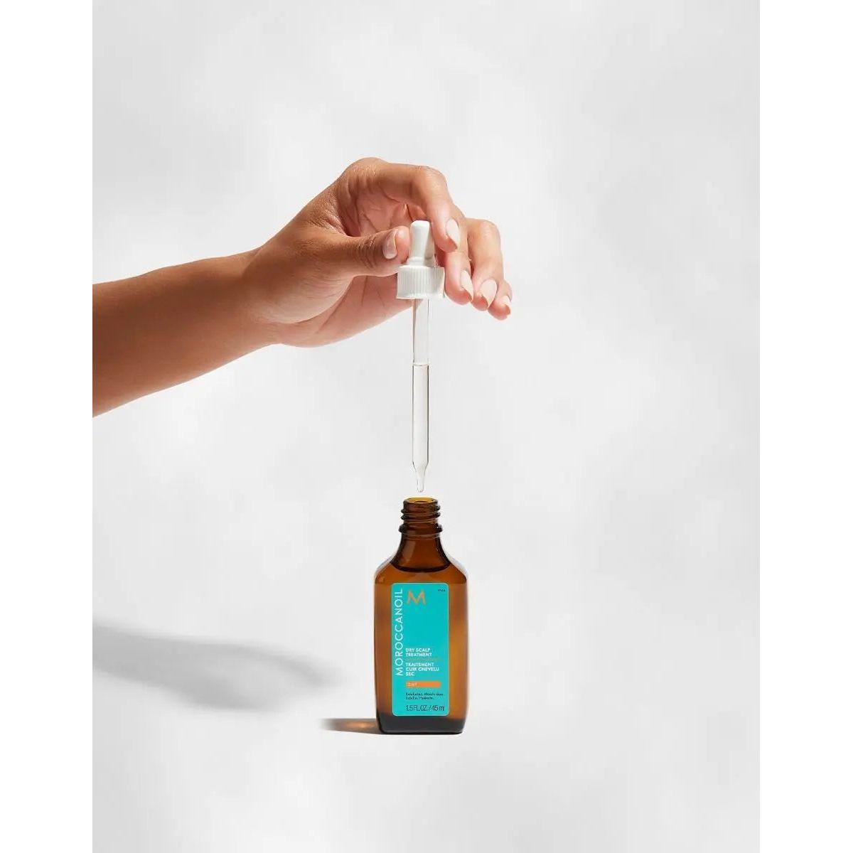 Hand holding a dropper filled with Moroccanoil Dry-No-More Scalp Treatment for dry scalp relief and hydration.