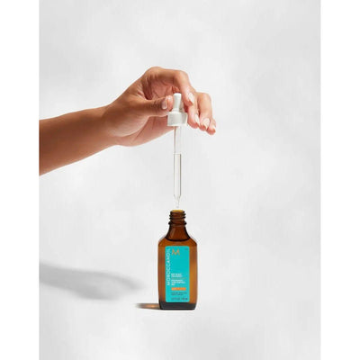 Hand holding a dropper filled with Moroccanoil Dry-No-More Scalp Treatment for dry scalp relief and hydration.