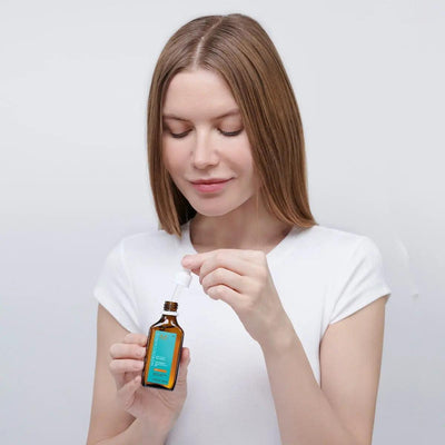 Woman applying Moroccanoil Dry Scalp Treatment with dropper for dry scalp relief and revitalizing hair.