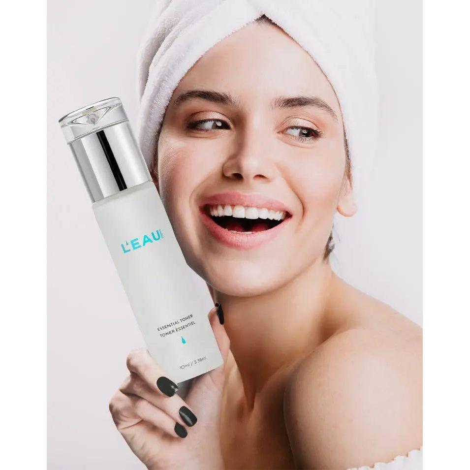Woman smiling while holding L'Eau Essential Toner, showcasing its rejuvenating and skin-tightening benefits.