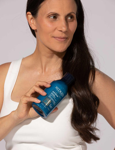 Woman holding Redken Extreme Shampoo 300ml, ideal for fortifying distressed and damaged hair.