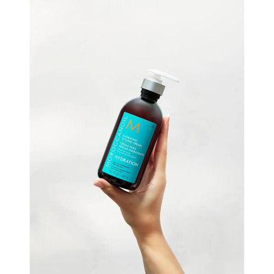 Moroccanoil Hydrating Styling Cream bottle held in hand, featuring conditioning and frizz-taming benefits for soft, shiny hair.