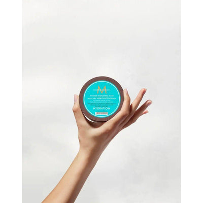 Hand holding Moroccanoil Intense Hydrating Mask jar, highlighting rich hydration for medium to thick, dry hair.