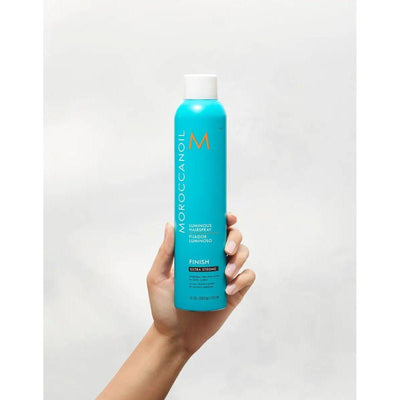 Luminous Extra Strong Finish Hairspray by Moroccanoil in hand, showcasing its bright turquoise packaging.