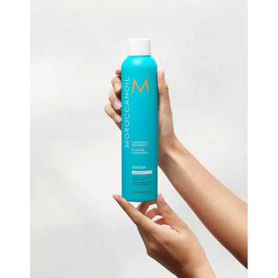 Moroccanoil Luminous Medium Finish Hairspray held in hand, showcasing its vibrant blue packaging and sleek design.