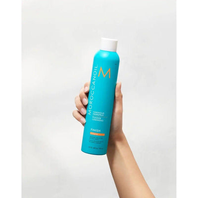 Hand holding Luminous Strong Finish Hairspray bottle with argan oil for flexible, long-lasting hold.