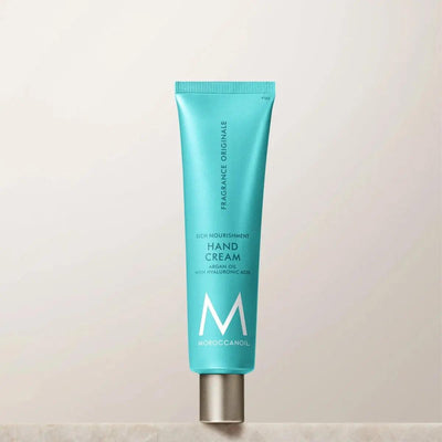 Moroccanoil Hand Cream featuring argan oil and hyaluronic acid in a turquoise tube on a neutral background.