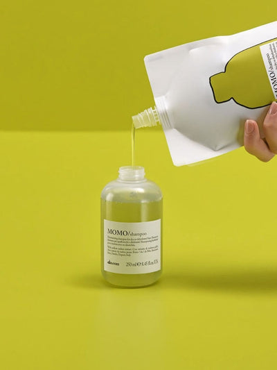 Momo Shampoo Refill being poured into a bottle on a vibrant green background, showcasing hydration for dry hair.