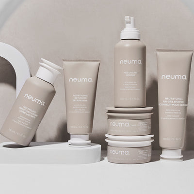 Neuma hair care products displayed on a modern surface, featuring styling clay, texture extender, and air-dry shampoo.