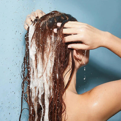 Woman applying Olaplex Nº.4 Bond Maintenance Shampoo to her wet hair in the shower, showcasing hydration and repair.