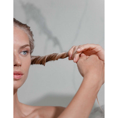 Woman with fine hair twisting a strand, showcasing the benefits of Kérastase Lait Vital Conditioner.