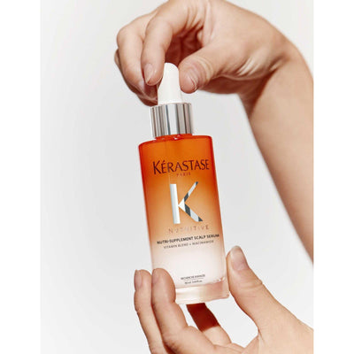 Kérastase Nutri-Supplement Scalp Serum in hands, moisturizing formula for dry scalps with niacinamide and vitamins.