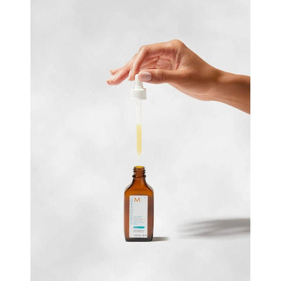 Hand holding a dropper above Moroccanoil Oily Scalp Treatment bottle, showcasing the product for oily scalp care.