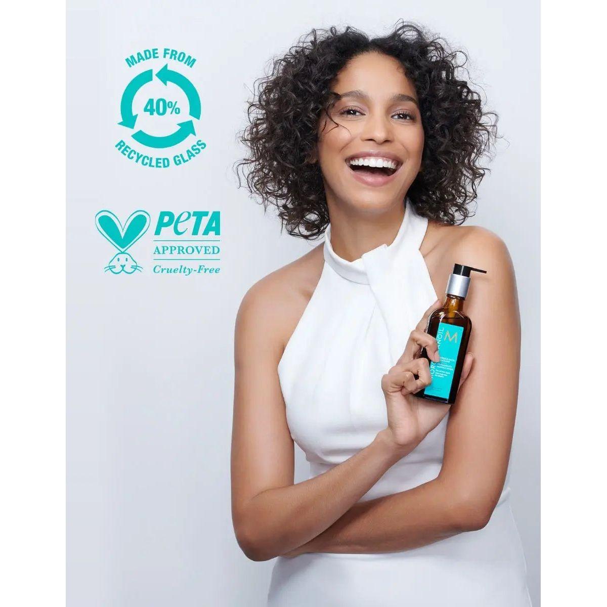 Model holding Moroccan Oil Original Hair Treatment in a bottle made from 40% recycled glass, showcasing PETA-approved cruelty-free product.