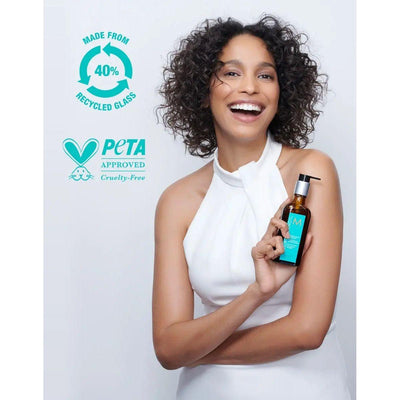 Model holding Moroccan Oil Original Hair Treatment in a bottle made from 40% recycled glass, showcasing PETA-approved cruelty-free product.