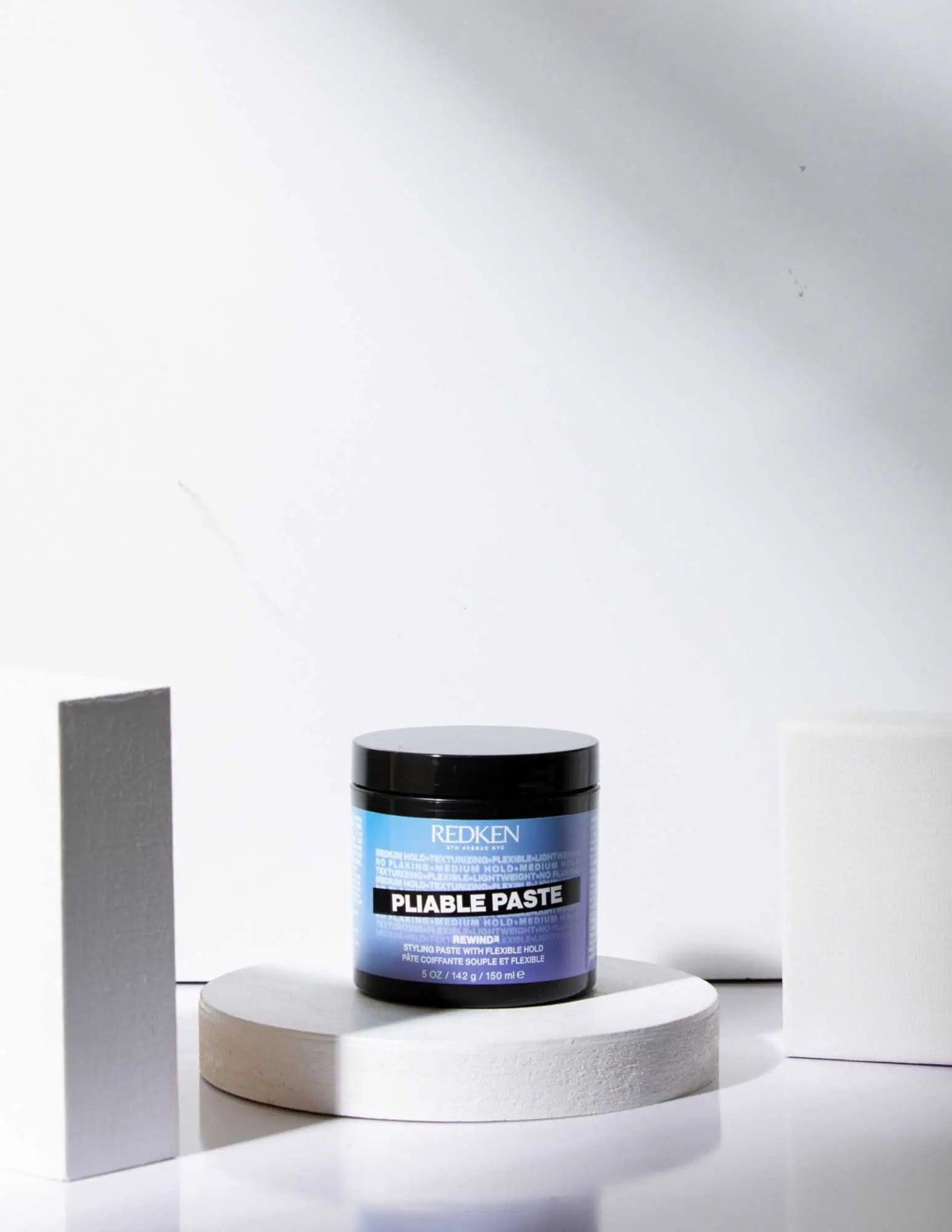 Redken Pliable Paste styling product in a jar, designed for flexible hold and versatile hairstyles, displayed on a minimalist background.