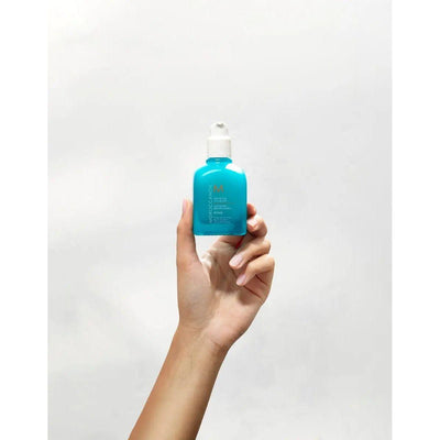 Hand holding Moroccanoil Mending Infusion bottle, a nourishing styling product for healthy, silky hair.