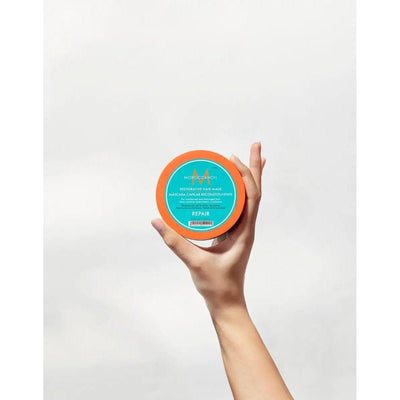 Hand holding a bright orange jar of Restorative Repair Hair Mask for deep hair repair and hydration.