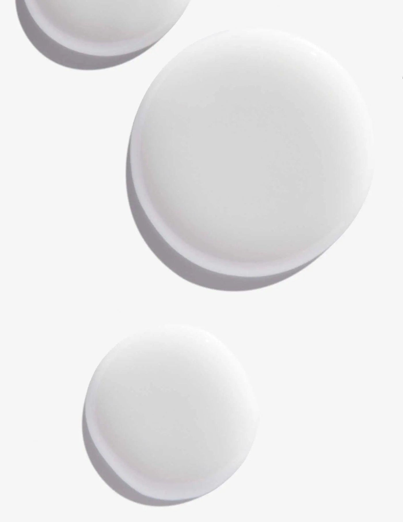 White round droplets of Scalp Relief Dandruff Shampoo on a light background, showcasing its smooth texture.