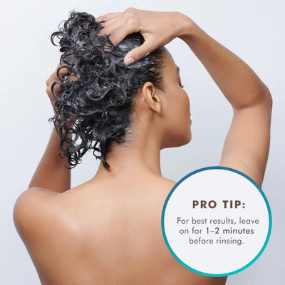 Woman applying Moroccanoil Smoothing Conditioner with curls, recommended to leave on for 1-2 minutes before rinsing.